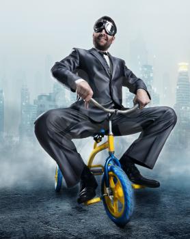 Odd businessman riding a small bicycle against dark city background