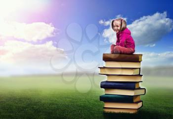 Cute, funny girl sits on the pile of books on nature background