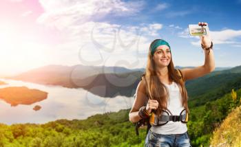 Pretty traveler woman with backpack is taking selfie on the top of mountain