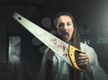 Scary portrait of an angry crazy woman with a bloody saw in her hand