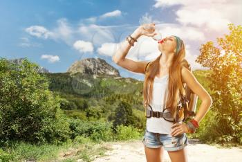 Hiking girl with backpack in the forest is drinking water