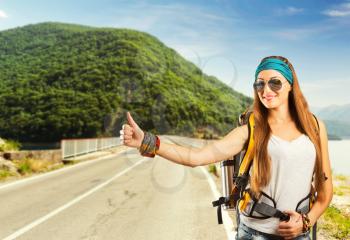 Happy traveler woman with backpack is catching a car on the road