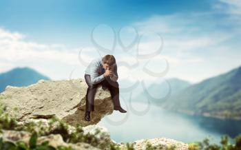 Frustrated businessman sits on edge of the cliff