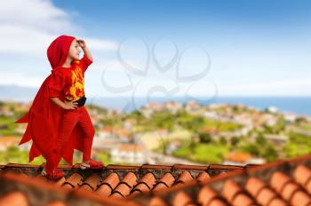 Little girl in a superhero costume standing on the roof