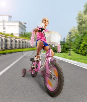 Cute little girl is cycling on pink bike on the street