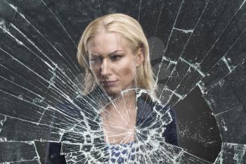 Depressed adult woman stands behind broken glass