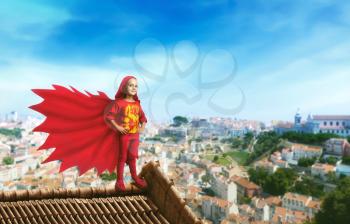 Little girl in a superhero costume standing on the roof against cityscape