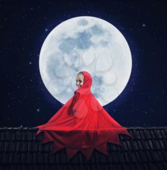 Little girl in a red gown over the moon in the night sitting on the roof