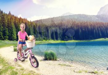 Cute little girl cycling on pink bike near the lake