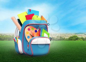 School backpack with books and pens on meadow against cityscape