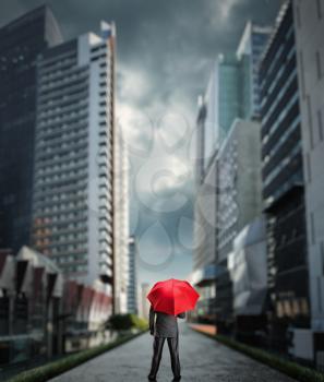 Businessman standing back with a red umbrella in the city