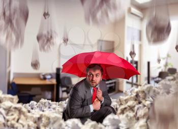 Scared businessman with umbrella protecting from papers in the office