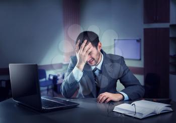 Frustrated businessman holding his head sits in the office at night