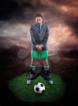 Businessman in sportwear protecting his genitals looks at the football