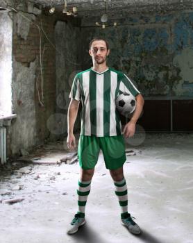 Football-player with a ball stands in an old room