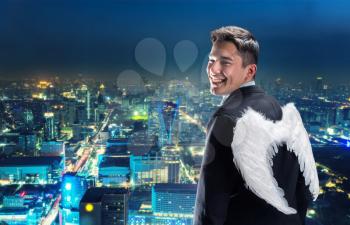Businessman with angel wings on his back looking at night city