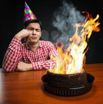 Sad birthday boy looking at the burning cake