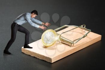 Businessman trying to pick a gold coin in the mousetrap