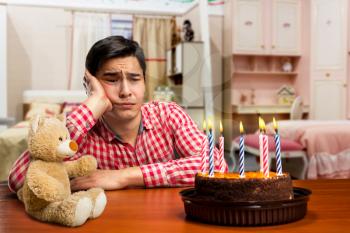 Sad birthday boy and cake with candle at the table 