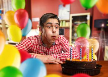 Birthday boy blowing out candles on the cake in decorated room
