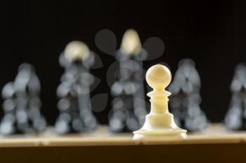 White pawn standing in front of the black chess team