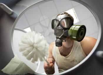 Man in gas mask with brush cleaning the toilet bowl