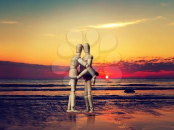 Couple of wooden figures hugging on the beach at sunset