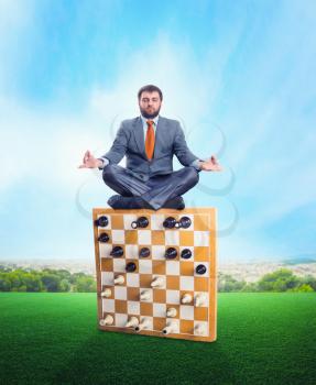 Businessman meditating sitting on the chess board edge