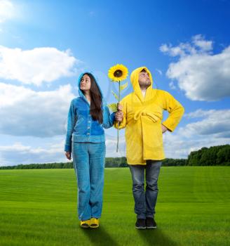 Woman in blue pijamas and man in yellow bathrobe holding sunflower on the meadow