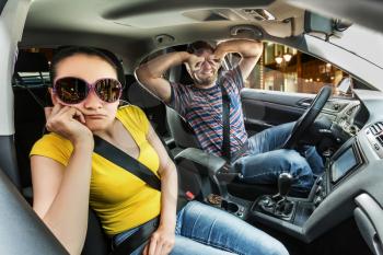 Couple in the car, man covering his eyes with hands, woman is scared
