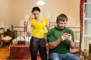 Adult man playing with his phone, wife in angry in the room