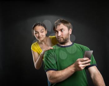 Man playing with phone, woman looking over the shoulder over black background