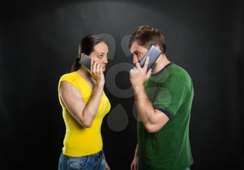Angry man and woman talking by mobile phones in the room