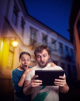 Very excited man and woman playing with tablet on the street in the evening