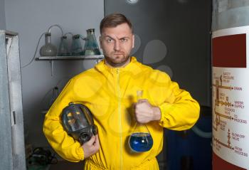 Man in protective outerwear suit stands with a flask with blue luquid