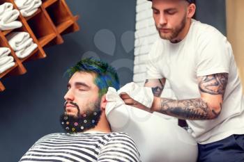 Young man has his hair colored in barber's shop, barber is wiping the head of his client with a towel