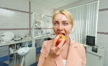 Young woman eating an apple in the dentist's office