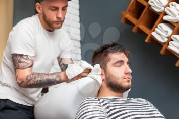 Young man has his hair washed in barber's shop, barber is wiping the head of his client with a towel