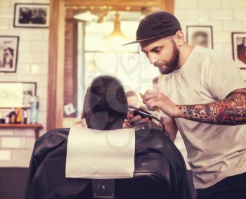 Young man having his beard shaven, barber working with trimmer in the salon