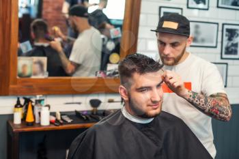 Cheereful young man having hair dress, barber working with hair clipper