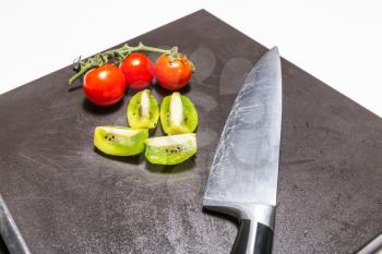 Knife, cherry tomatoes and sliced kiwi fruit on the board