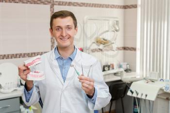 Happy dentist in the office with instruments and artificial jaws