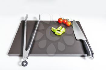 Knife, holder, cherry tomatoes and sliced kiwi fruit on the board