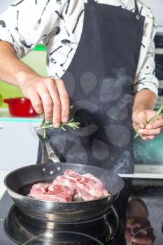 Man adding rosemary to meat on the frying pan