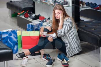 Young woman sitting on the floor in the shoe store thinks over what shoes to choose