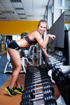 Side view of smiling young girl exercising with dumbbells in the gym in front of the mirror