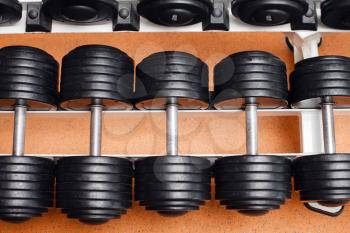 Heap of black dumbbells with weight plates on the rack