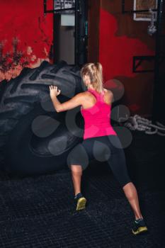 Young girl exercising with a big tire in the gym