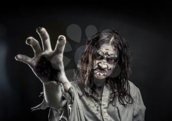 Horror zombie woman with bloody face reaching hand to you