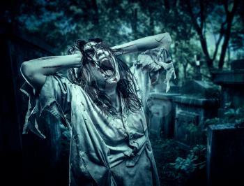 The shouting female zombie against the background of the cemetery. Horror. Halloween.